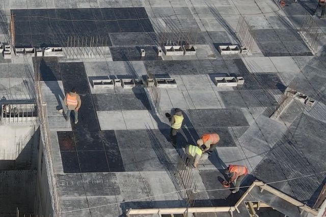 A crew in orange vests working on the top floor slab among rebar and formwork.
